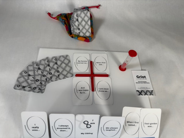 Griot game cards set up for play. Black and white cards. Red sand timer and card divider. Colorful bag under card deck